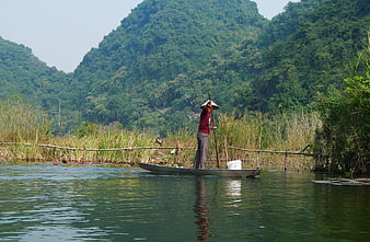 Vietnamese fisherman in conical hat rowing boat on river