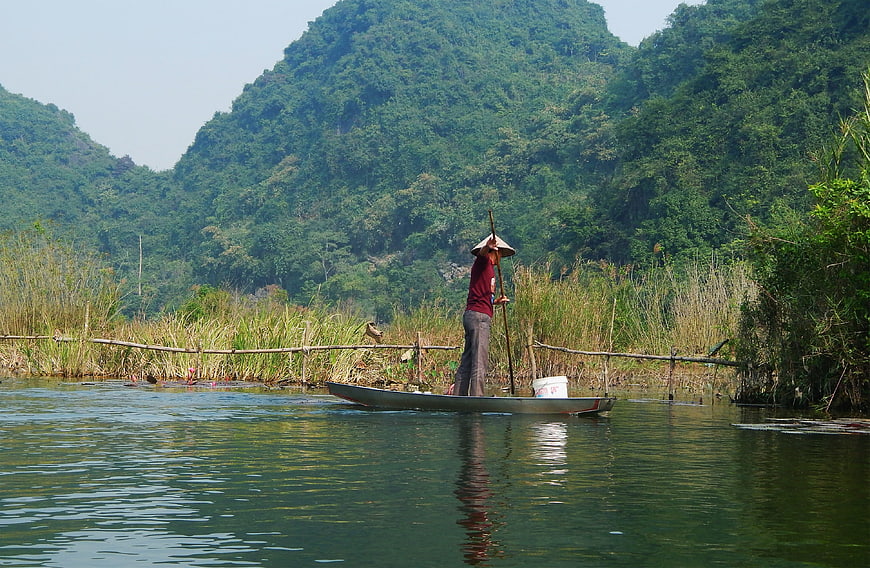 Vietnamese fisherman in conical hat rowing boat on river
