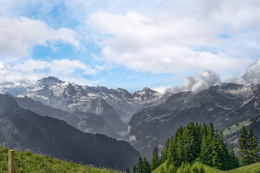 Majestic Alpine Mountain Range Panorama With Snowy Peaks And Green Forestry
