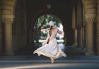Indian woman dancing in traditional attire under stone arches