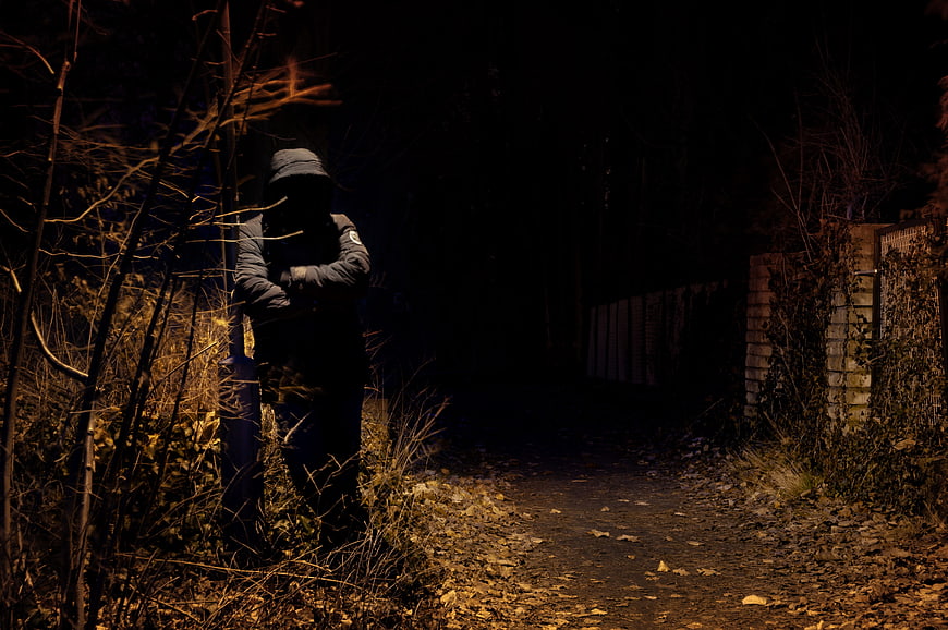 Mysterious hooded figure standing in dark forest at night