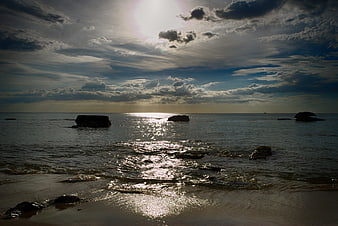 Dramatic sunset over ocean with silhouetted rocks and clouds