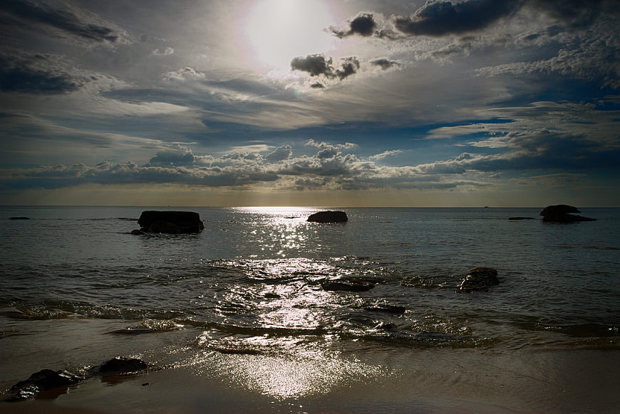 Dramatic sunset over ocean with silhouetted rocks and clouds