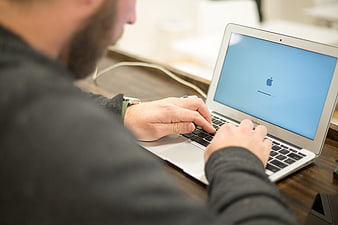 Man Typing on Laptop at Wooden Desk