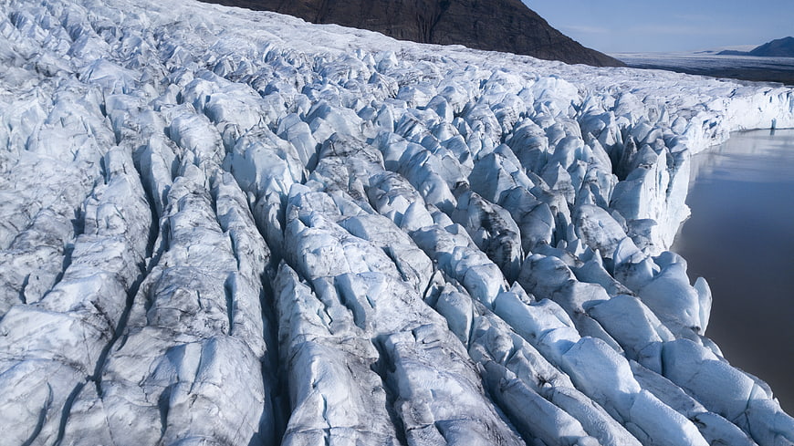Aerial view of textured glacier ice meeting calm water