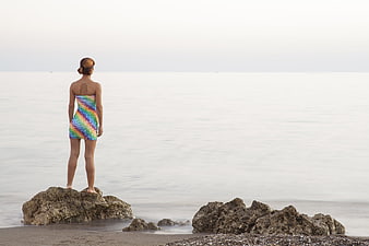 Woman in colorful dress standing on rocks by the sea