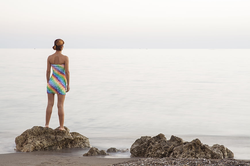 Woman in colorful dress standing on rocks by the sea