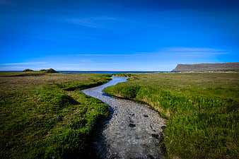Winding Stream Through Green Grassland to Ocean Horizon