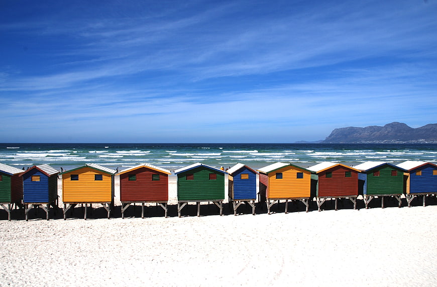 Colorful Beach Huts on Sandy Shore with Ocean and Mountains
