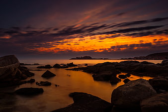Dramatic Orange Sunset Over Rocky Coastal Shoreline