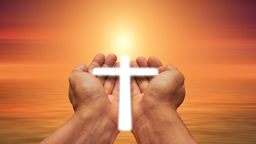 Hands holding glowing white cross against warm sunset background