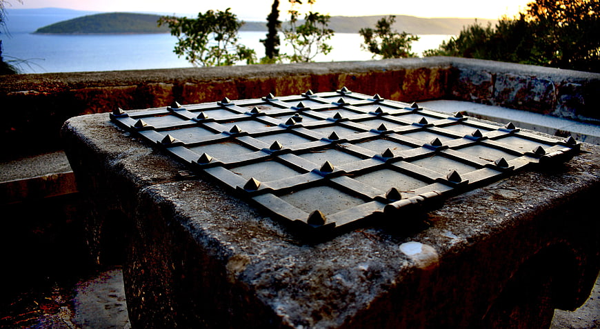 Rusty Metal Grid Cover On Stone Well With Coastal View