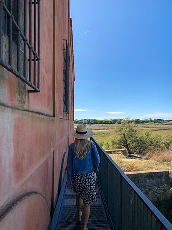 Woman in straw hat walking on metal walkway near pink building