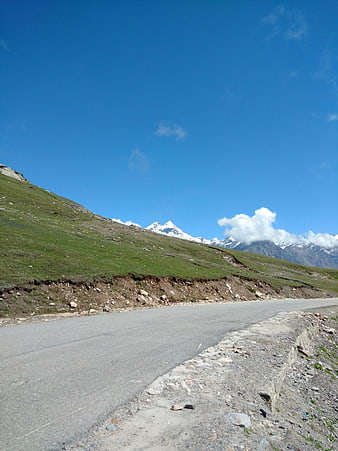 Paved mountain road with green slopes and snow-capped peaks