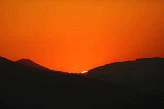 Silhouette of mountains against vibrant orange sunset sky