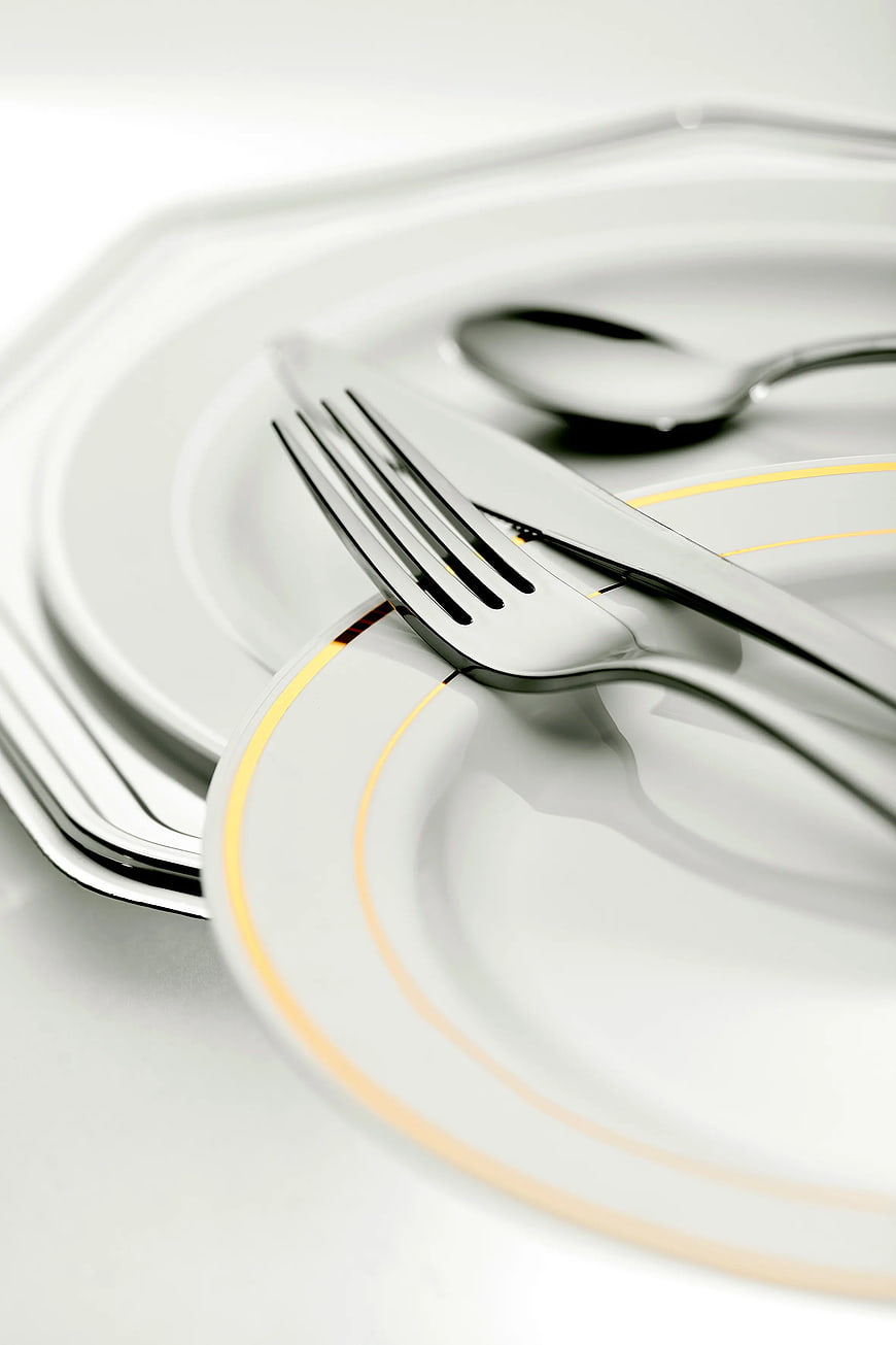 Close-up of elegant white plates with gold rim and silver cutlery