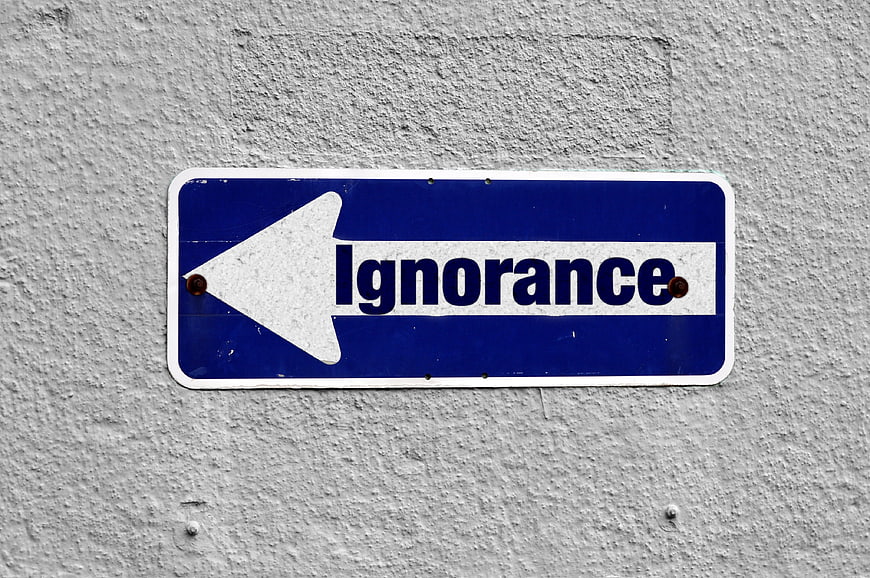 Blue street sign pointing left with word ignorance