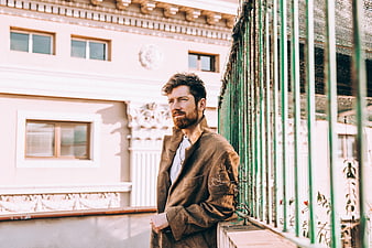 Handsome Bearded Man in Brown Coat Leaning on Green Railing