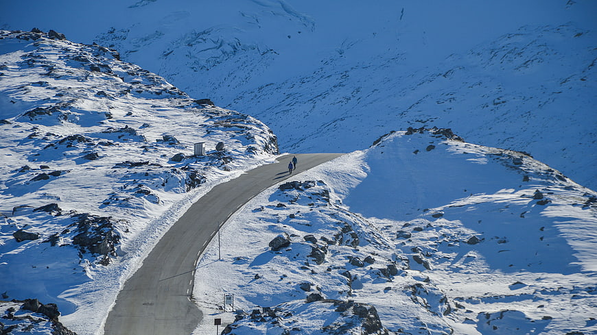 Hikers walking on winding snowy mountain road