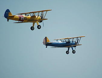 Two vintage biplanes flying in formation against blue sky