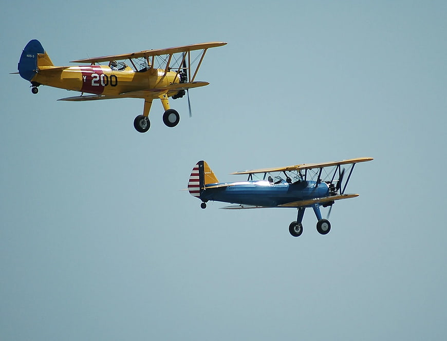 Two vintage biplanes flying in formation against blue sky