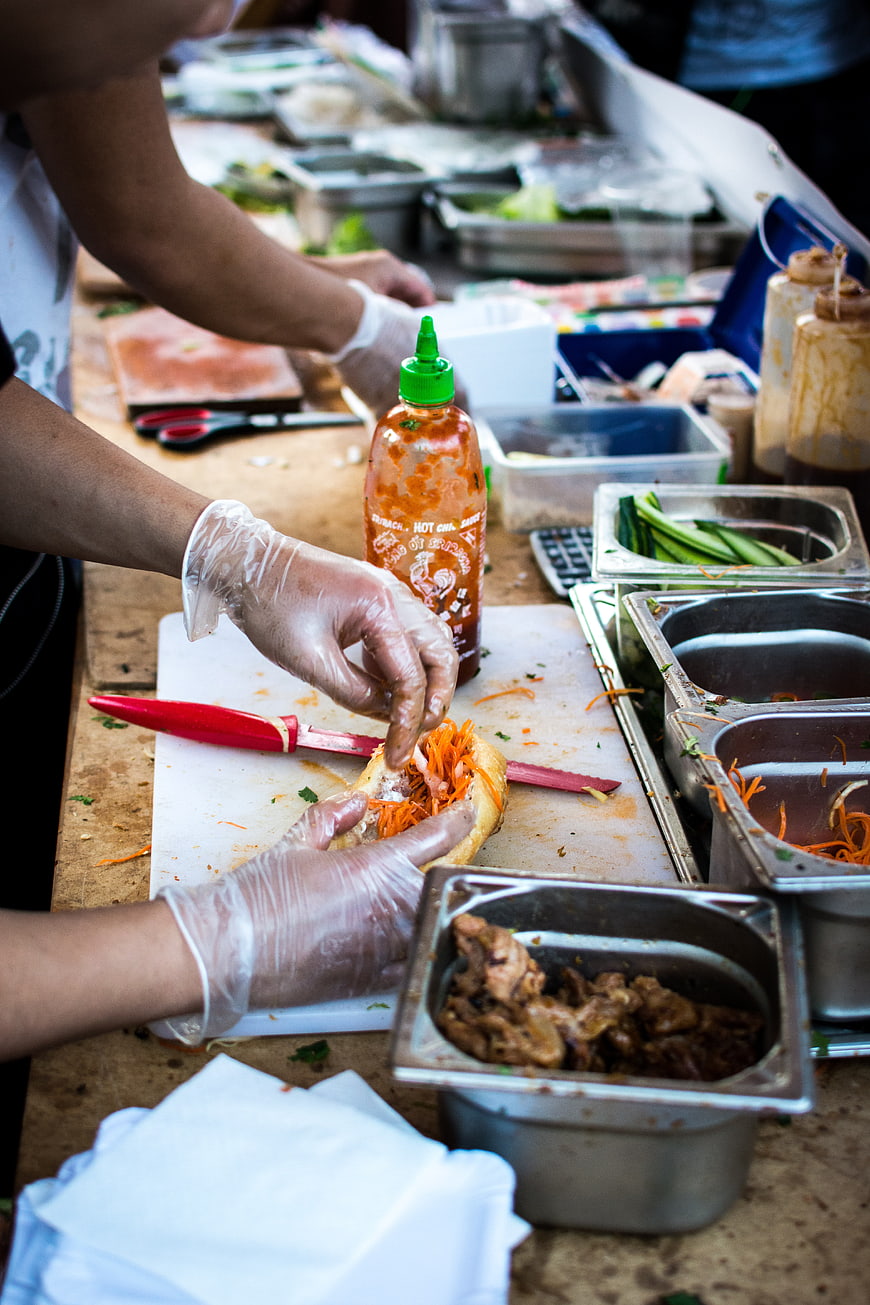 Hands preparing Vietnamese Banh Mi sandwich with fresh ingredients