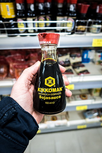 Hand holding Kikkoman soy sauce bottle in supermarket aisle