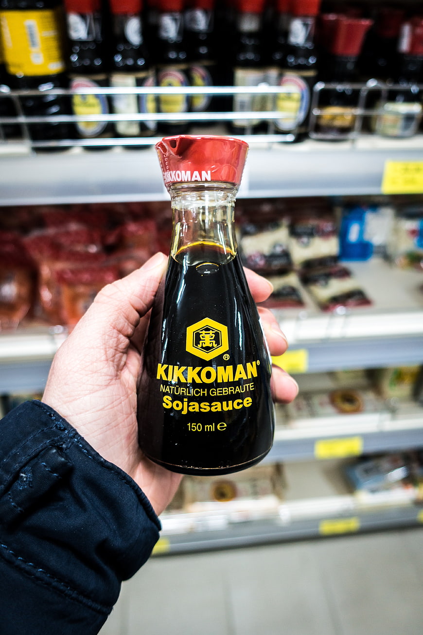 Hand holding Kikkoman soy sauce bottle in supermarket aisle