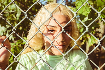 Blonde woman looking through chain link fence in sunlight