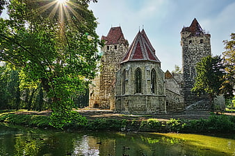 Historic Stone Castle Ruins With Red Roofs Beside A Green Pond
