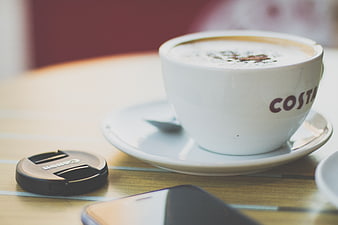 Costa Coffee Cup with Camera Lens Cap on Wooden Table