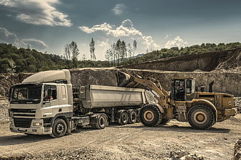Yellow Wheel Loader Loading Gravel into White Dump Truck at Quarry