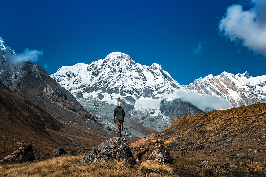 Lone Hiker Standing on Rock Facing Snowy Mountain Peak