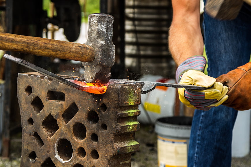 Blacksmith Forging Hot Iron with Hammer and Tongs in Workshop