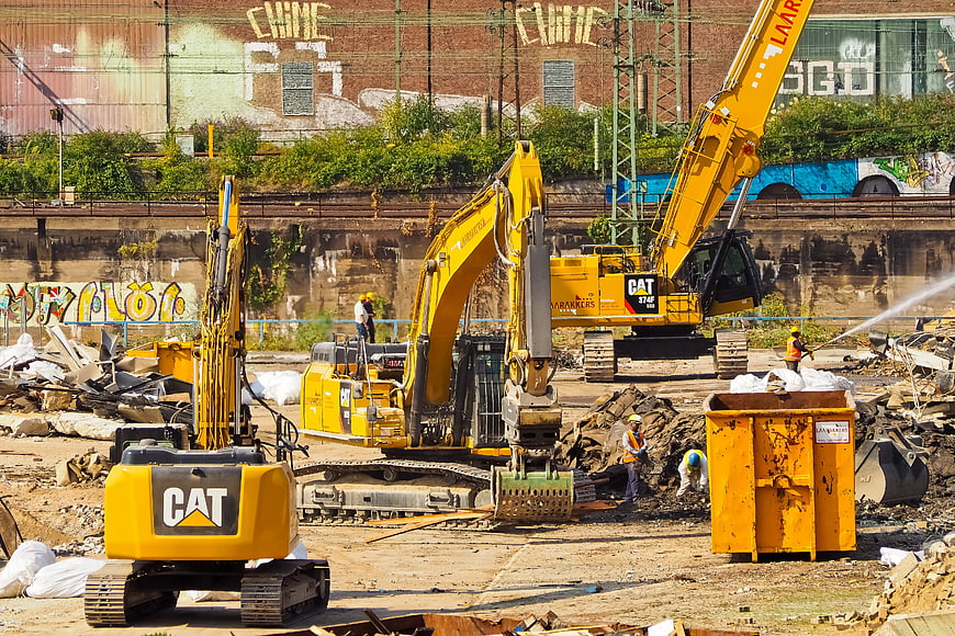Yellow CAT Excavators Demolishing Building With Workers And Rubble