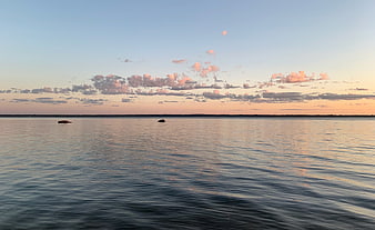 Serene sunset over calm sea with pink clouds and distant horizon