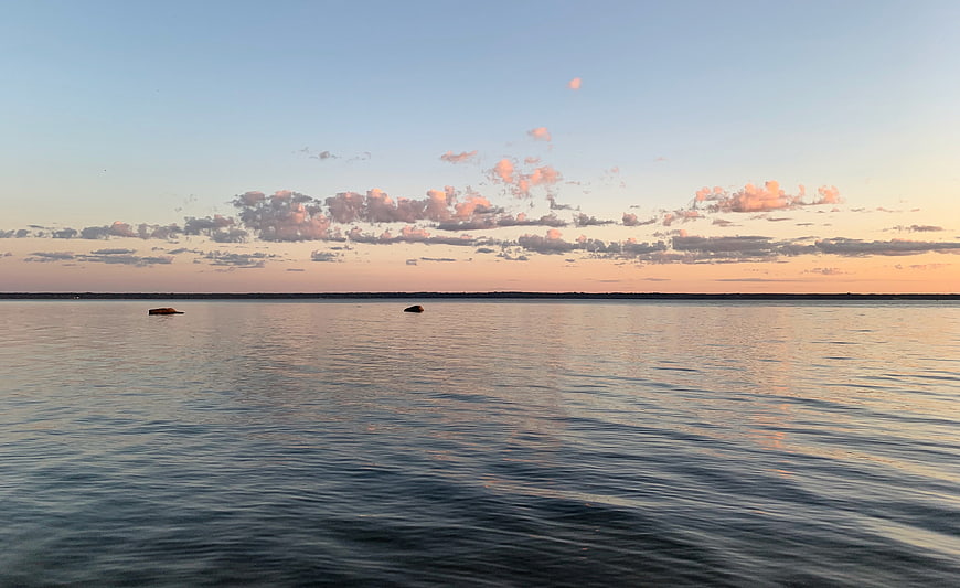 Serene sunset over calm sea with pink clouds and distant horizon