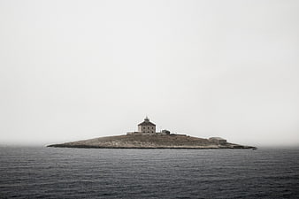 Lighthouse on small island in foggy sea