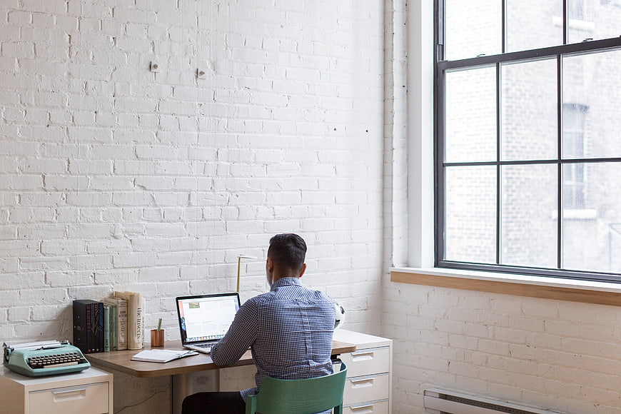 Man working at desk in bright loft office with white brick wall