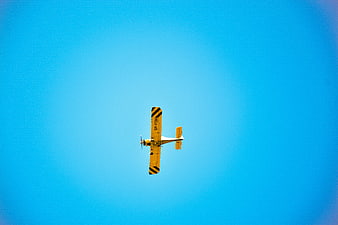 Yellow biplane flying against a clear blue sky