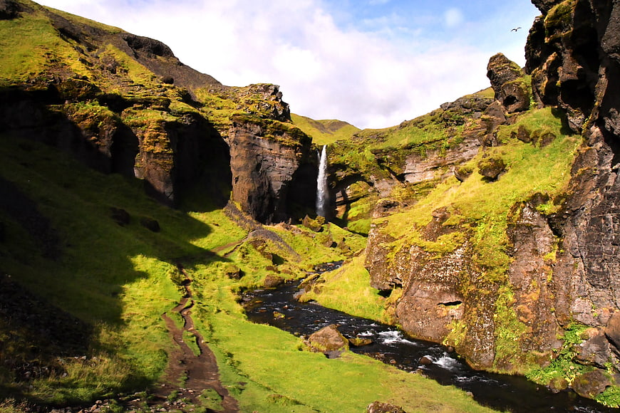 Scenic waterfall cascading into a river in a lush green Icelandic valley
