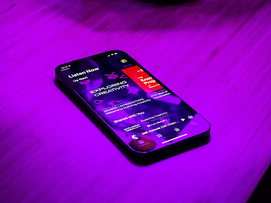Smartphone displaying podcast app on purple wooden table