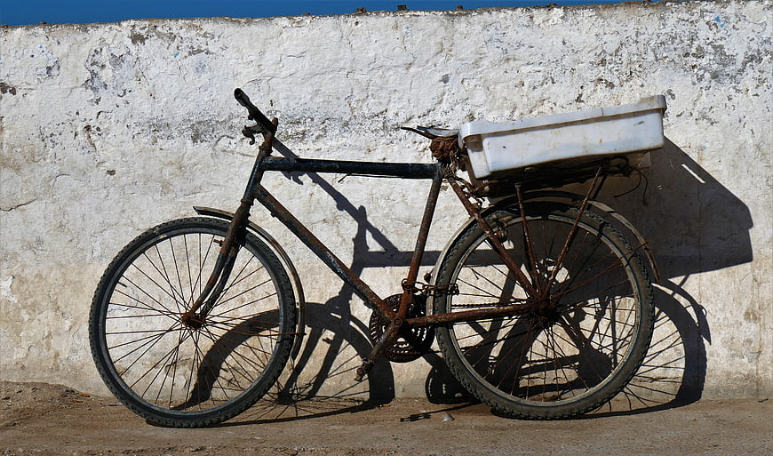 Rusty vintage bicycle with white box against textured wall