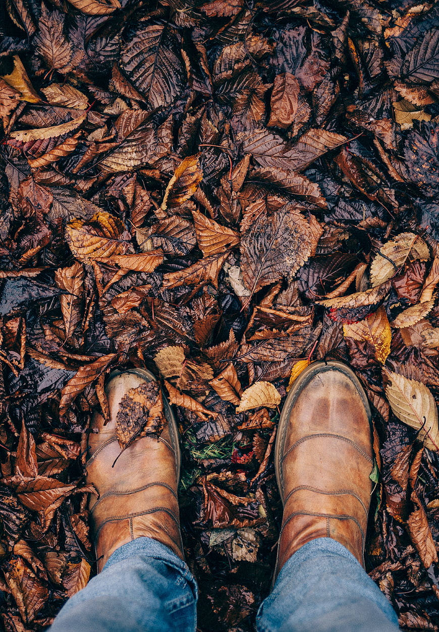 First-person view of brown leather boots on wet autumn leaves
