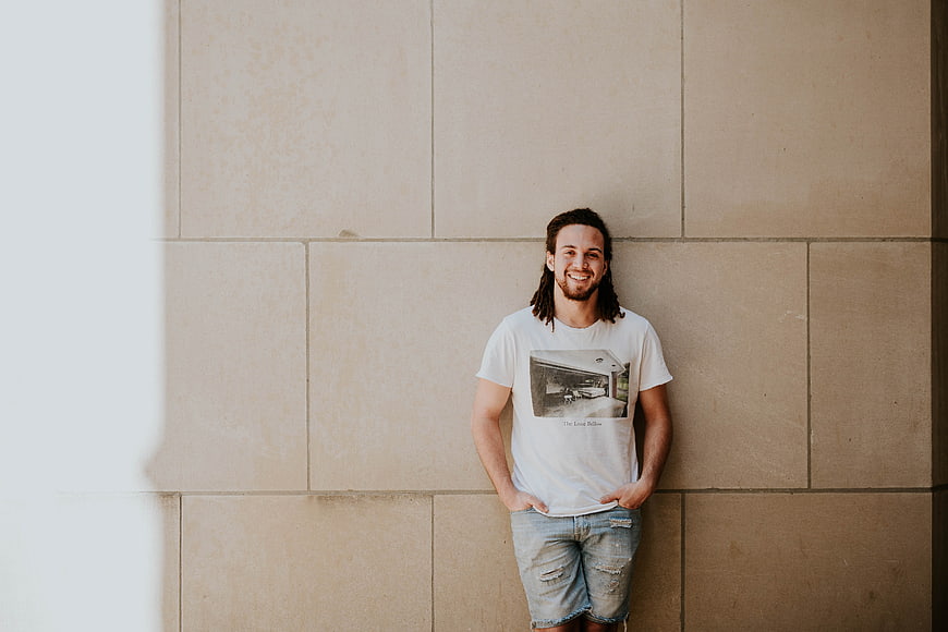 Happy Man with Dreadlocks Leaning Against Beige Wall