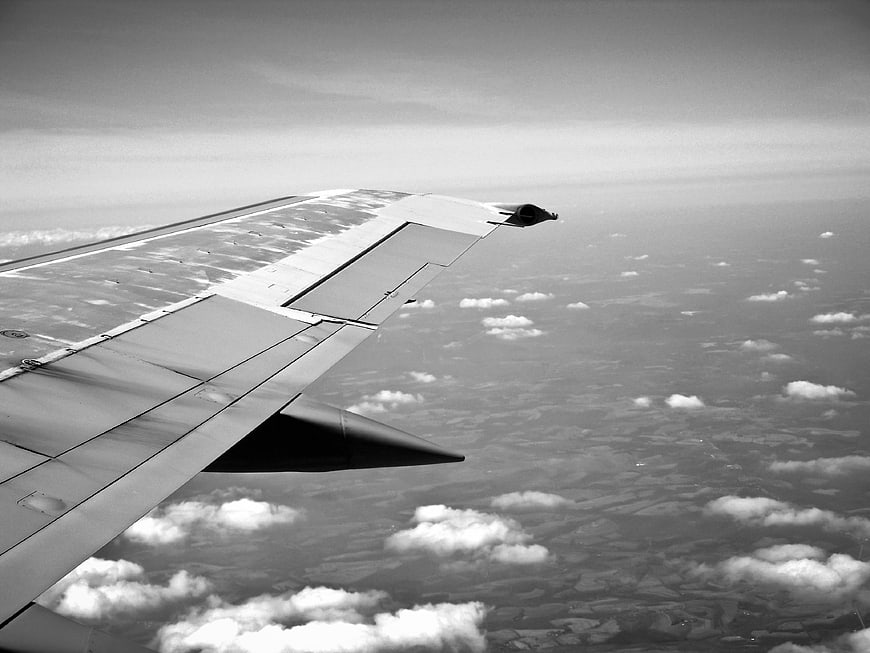 Black and white airplane wing view above clouds