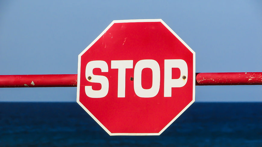 Red Stop Sign on Barrier Against Blue Ocean Sky