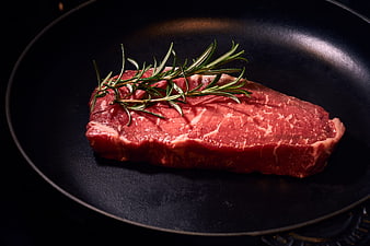 Raw Beef Steak With Fresh Rosemary Sprig On Black Cast Iron Pan