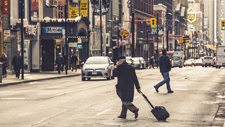 Senior man with suitcase crossing busy city street