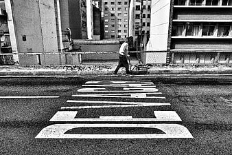 Black and white street photography of man walking on scooter